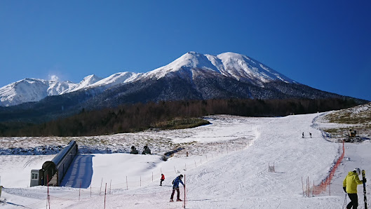 View of the Kaida Kogen Mia ski resort in Nagano, Japan with a winter sports scene featuring skiers on a mountain slope. A cozy chalet is nestled at the foot of the mountain, completing this picturesque winter landscape.