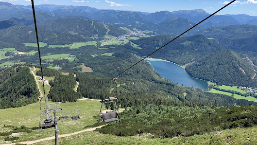 A scenic view from Gemeindealpe Mitterbach in Lower Austria showcasing a bustling ski resort complete with a visible ski lift. A chalet can be glimpsed in the distance next to the snowy mountain.