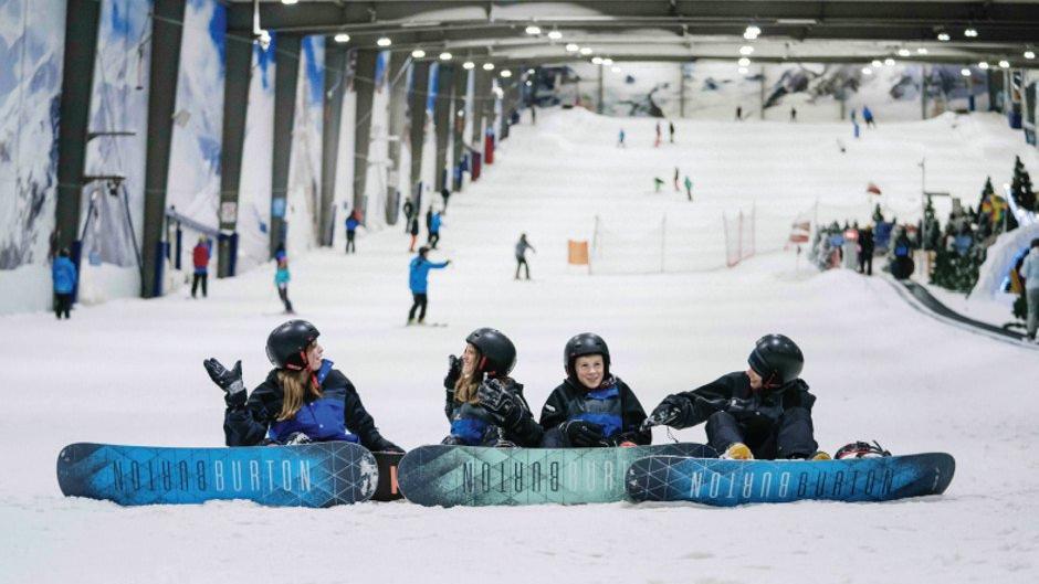 Snowplanet – Silverdale in New Zealand - two people sitting on snowboards in the middle of a ski slope.