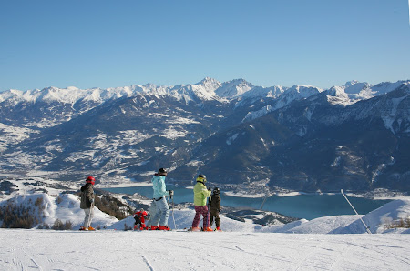A scenic view of Réallon ski resort in France featuring a charming chalet and a group of people engaged in winter sports with a skier prominently featured.