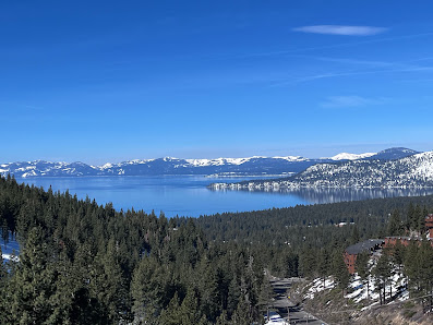 Scenic view of Diamond Peak in Lake Tahoe Incline Village Nevada displaying a glistening lake surrounded by sunlit snow-covered mountains highlighting a winter sports scene on a bright day.