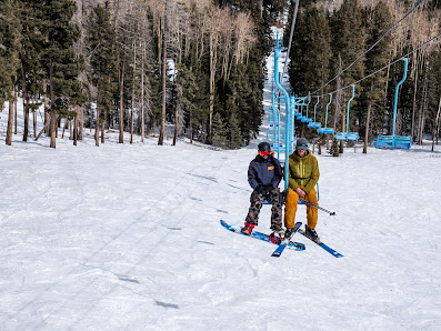 A skier and a family are enjoying winter sports on Pajarito Mountain in Los Alamos New Mexico. They are ascending the mountain on a ski lift to participate in activities at the frosty ski resort.