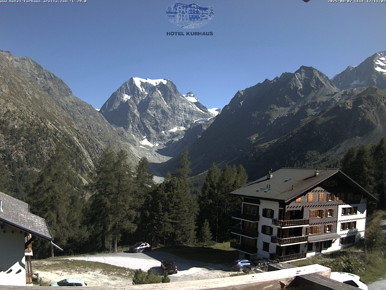 View of a chalet nestled in the breathtaking winter scenery of Arolla, Switzerland. Features include a ski resort and a lively winter sports scene, with a commanding mountain in the backdrop.