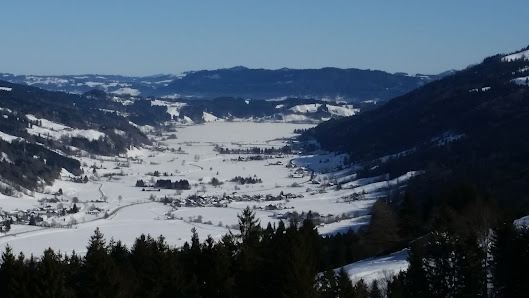A scenic winter view at Hündle ski resort in Germany featuring a chalet nestled amidst snowy mountains with people engaging in winter sports.
