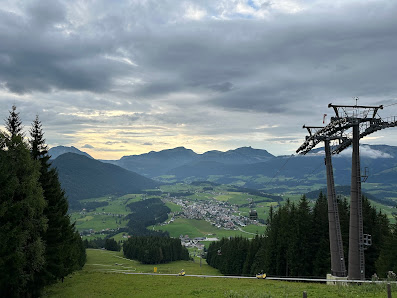 A picturesque view from Karkogel - Abtenau ski resort in Austria featuring a cosy challet and a ski lift ascending towards the vast mountain. A mountain bike is also present suggesting multi-seasonal activities.