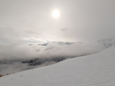 View of Pelvoux Vallouise in France featuring a towering snow-covered mountain, a lively ski resort with a charming chalet, and a skier coasting along.