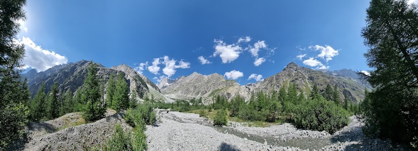 View of Pelvoux Vallouise in Hautes-Alpes, France, with a charming chalet nestled at the base of a grand mountain on a sunny day; a peaceful lake is in nearby proximity.