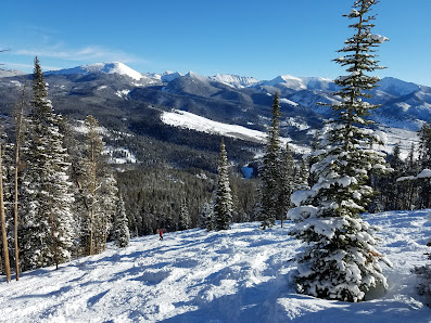 A winter sports scene at Maverick Mountain ski resort in Polaris Montana featuring a skier in motion against a backdrop of snow-capped mountains and scenic winter surroundings.