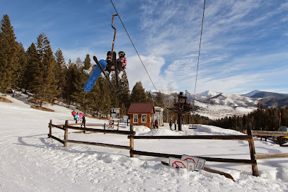 A scenic view of Maverick Mountain in Polaris Montana showcasing a bustling winter sports scene. Visible elements include a ski lift carrying outdoor enthusiasts up the snow-covered mountain and skiers enjoying the slopes.