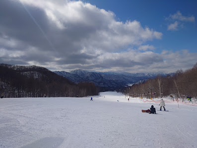 Winter sports enthusiasts enjoying a day at the Aizu Kogen Takatsue ski resort in Tōhoku, Fukushima, Japan, with a charming chalet and stunning snow-covered scenery around.