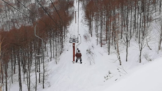 A skier gliding down the slopes at Aizu Kogen Takatsue in Tōhoku, Fukushima, with a ski lift in view, illustrating a vibrant winter sports scene in Japan.