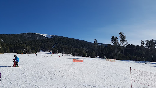 A lively scene at Cambre d'Aze – Eyne ski resort in France featuring a skier in motion a ski lift and a bustling winter sports centre amidst pristine snow.