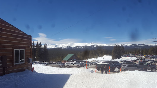 View of a ski resort at Cooper in Leadville, Colorado, featuring a bustling winter sports scene. A ski lift and a challet rests amidst the panoramic view of a majestic mountain blanketed with thick white snow.