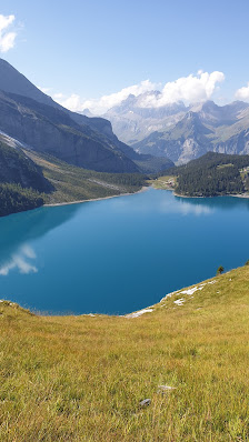 View of the serene Oeschinensee Lake in Switzerland's Bernese Oberland, complete with a quaint challet nearby, set against the awe-inspiring backdrop of towering mountains.