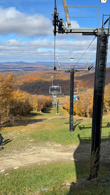 A vibrant wintery scene at Mont Sutton Quebec featuring a ski lift ascending a snowy mountain skiers enjoying the snowy slopes and a cozy chalet nestled in the picturesque backdrop.