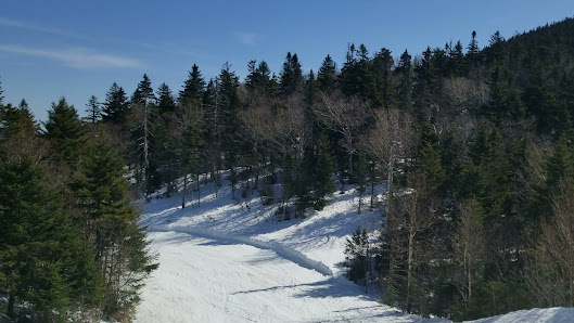 Winter scene at Mont Sutton in Quebec, Canada showcasing a bustling ski resort with skiers using the ski lift and descending down the snow-covered slopes.
