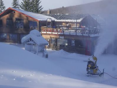 Winter sports enthusiasts enjoying a day at Mont Sutton, a ski resort in Sutton, Quebec, Canada. The image includes a busy ski slope, ski lift, and snowmobile amidst snow covered surroundings.