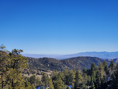 A sunny day at Mt. High East in Wrightwood California showcasing the picturesque mountain scenery. A chalet and ski resort are nestled on its slopes and a mountain bike rests nearby.
