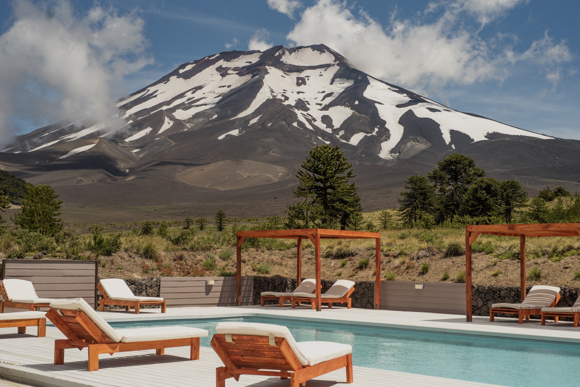 View of Corralco in Araucanía, Chile showing a lodge and chalet nestled at the base of a snowy mountain, which is part of a serene ski resort. The vast mountain dominates the landscape.