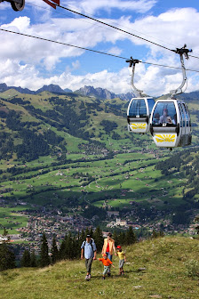 Ski lift ascending the snowy slopes at Wispile-Gstaad ski resort in Switzerland under a bright, sunny sky. A charming chalet can be seen in the background, and a skier enjoys the terrain.