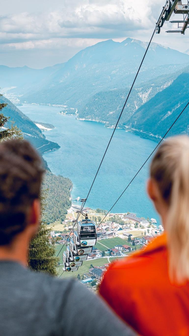 Karwendel Bergbahn – Pertisau in Austria - a man and woman sitting on a chair looking at a view of a lake and mountains.