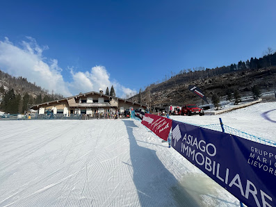A view of LeMelette – Gallio a ski resort in Vicenza Italy showcasing a winter sports scene with a chalet in the distance and a skier on the snow-covered slopes.