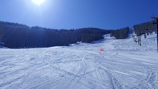 A skier navigates a winter sports scene at Sunlight Mountain a ski resort in Glenwood Springs Colorado. A chalet and snowmobile are visible amidst the snowy landscape.