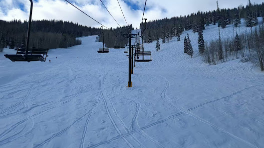 A skier enjoying a beautiful day at Sunlight Mountain ski resort in Glenwood Springs, Colorado. A ski lift ascends the snowy mountain, tucked among the sparkling white landscape, delivering winter sports enthusiasts to their next adventure.