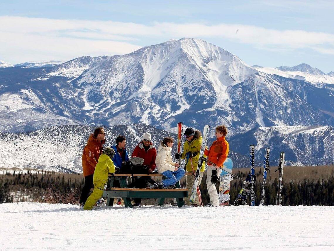 Sunlight Mountain in USA - a group of people sitting on top of a snow covered hill.