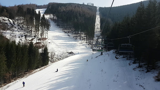Ski resort in Kouty nad Desnou, Czech Republic, featuring a busy winter sports scene. Skiers are visible enjoying the slopes, while others take the ski lift up the mountain.