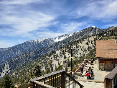 A photograph capturing the stunning landscape of Mt Baldy, California. Dominating the image is a welcoming ski resort and lodge nestled near a mountain hut, surrounded by the serene beauty of the massive, snow-capped mountain.