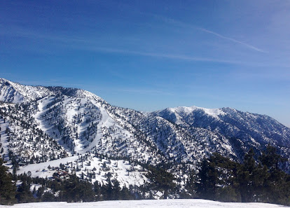 Winter sports enthusiasts enjoying the snowy slopes of Mt. Baldy in California, with a charming chalet nestled at the foot of the mountain offering a striking winter scenery view.