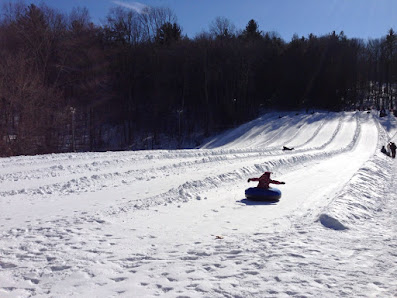 A bustling winter sports scene at Butternut in Great Barrington Massachusetts featuring a snowmobile skiers and a challet amidst an expansive winter sports centre.