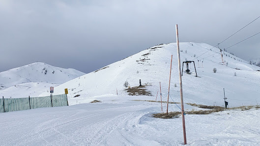 View of Obertilliach-Golzentipp ski resort in Austria, featuring a winter sports centre, a populated ski lift, and a distant chalet amid a scenic snow-covered landscape.