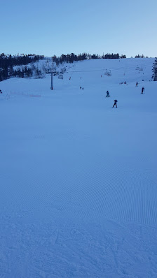 Skiers enjoy the slopes at Gautefall Skisenter in Telemark, Norway. The scene features a bustling ski resort, a ski lift and a charming challet nestled amongst the snow-clad mountains.