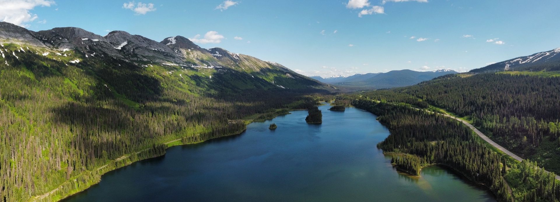 A scenic view at Powder King in Northern British Columbia Canada featuring a sizable lake bordering a mountain range a distant ski resort and a chalet all bathed in the light of a sunny day.