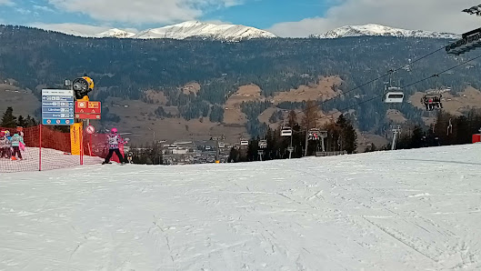 A skier zooms down the Baranci Piste Da Sci at the 3 Zinnen Dolomites ski resort in South Tyrol, Italy, surrounded by winter scenery with a chalet and ski lift in the background.