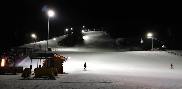 Skier descending a snow-laden hill at Baranci Piste Da Sci in Italy, with ski lifts and winter sports activities bustling around the ski resort.