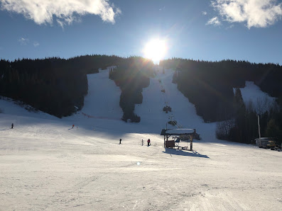 Ski resort at Purden Ski Village in British Columbia, Canada featuring a busy winter sports scene on a glistening mountain slope. A ski lift is visible, leading up to a quaint chalet nestled in the snow capped peak.