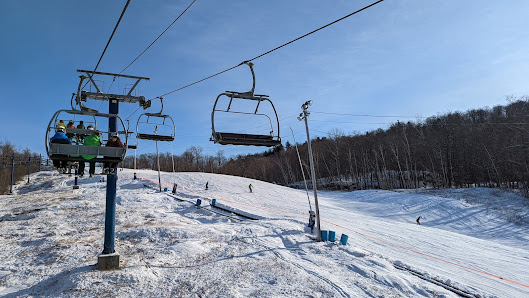 A winter sports scene at Camp Fortune in Chelsea Quebec showcasing a ski lift with a skier surrounded by a ski resort including a chalet.