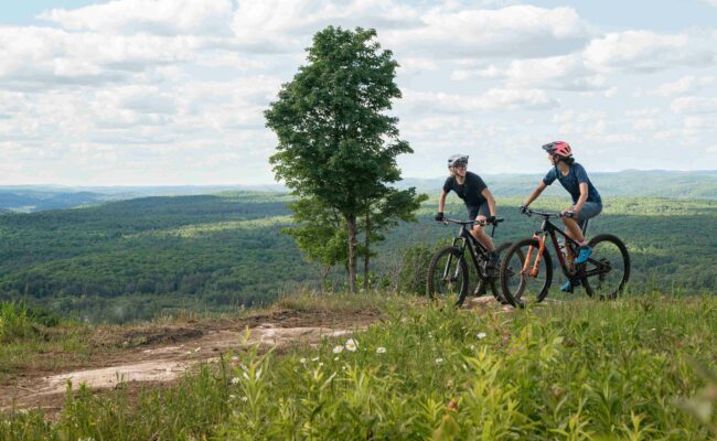 A mountain biker enjoying a ride at Camp Fortune in Chelsea, Quebec, Canada, with a small glimpse of a chalet in the backdrop.