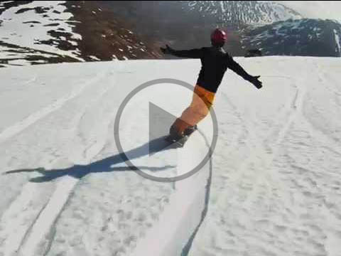 A skier and a snowboarder enjoying winter sports at Glencoe Mountain in Scotland, with a challet in the backdrop.