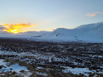 Winter scene at Glencoe Mountain in the Scottish Highlands, featuring snowy peaks, skiers enjoying winter sports, and a small chalet nestled against the mountains.