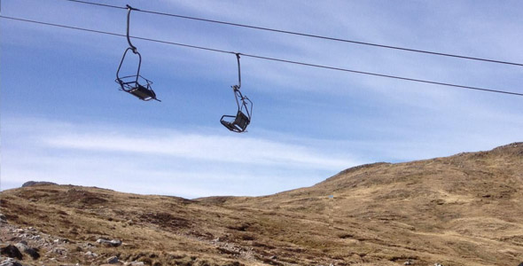 Skier rides a ski lift ascending Glencoe Mountain, in Scotland. The wintry scene showcases a ski resort backdrop, complete with a quaint chalet nestled among the White Corries.