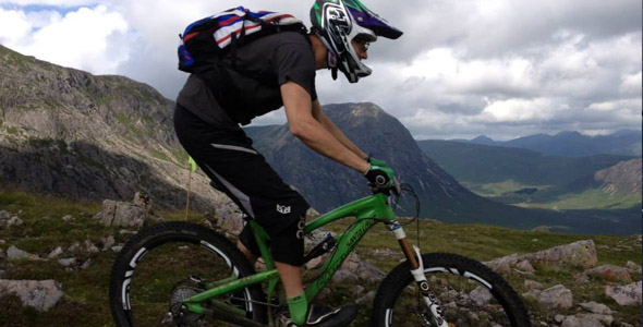 A mountain biker enjoys a thrilling ride on the trails of Glencoe Mountain in the Scottish Highlands with a chalet subtly nestled in the background.