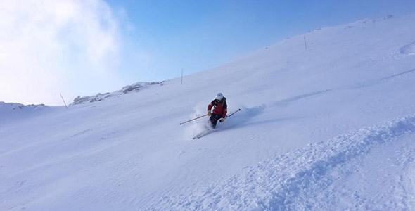 A skier sliding down the snow-covered slopes of Glencoe Mountain in Scotland, with a charming chalet and the bustling winter sports centre of the ski resort visible in the backdrop.