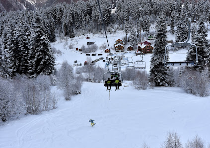 A winter scene at Hatsvali-Mestia ski resort in Georgia with a ski lift in view. People are enjoying winter sports amidst the snow-covered landscape and a challet is visible in the distance.