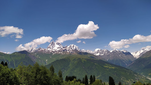 A picturesque view at Hatsvali Mestia in Ieli Georgia featuring a chalet nestled amidst majestic mountains dominated by snow-covered peaks. The serene mountainous landscape subtly hints at the presence of a ski resort.