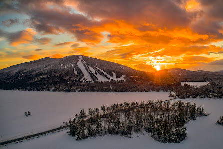 A winter sports scene at Pleasant Mountain in Bridgton Maine. The picture includes stunning winter scenery of a ski resort nestled in the heart of the mountain under a clear sky.