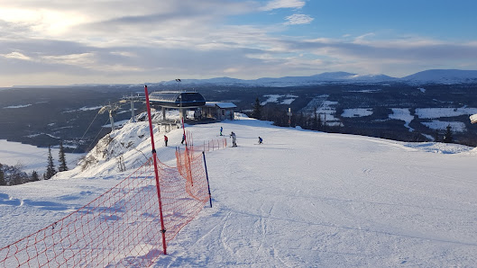 A winter sports scene at Funäsdalsberget in Northern Sweden featuring a ski resort with a ski lift in operation and a skier enjoying the slopes.